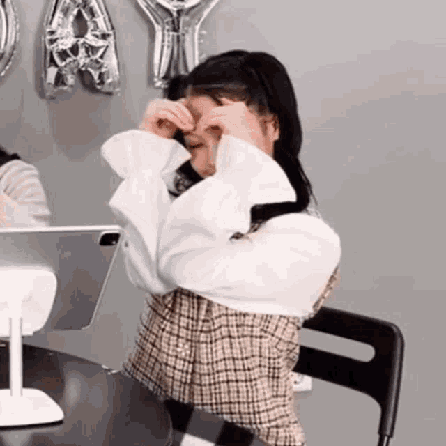 a girl is sitting at a table covering her eyes