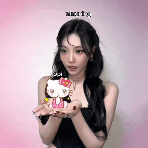 a girl holding a hello kitty in her hands with ningning written on the bottom right
