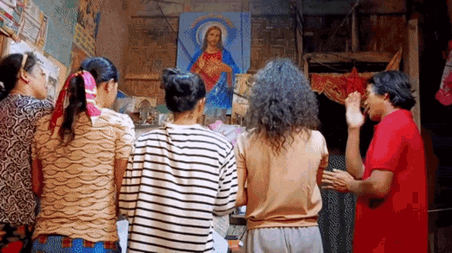 a group of women are standing in front of a painting of jesus on a wall .