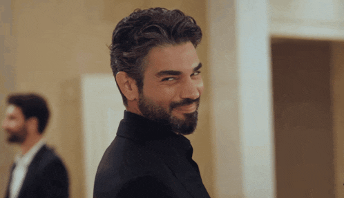 a man with a beard wearing a black suit smiles for the camera