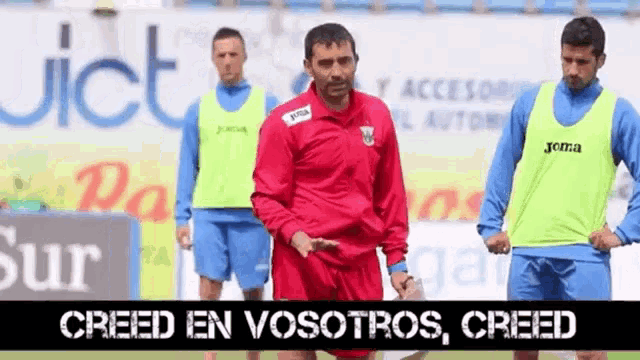 a man in a red jacket and blue shorts stands in front of a sign that says creed en vosotros creed