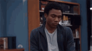 a man is sitting in front of a bookshelf and making a funny face .