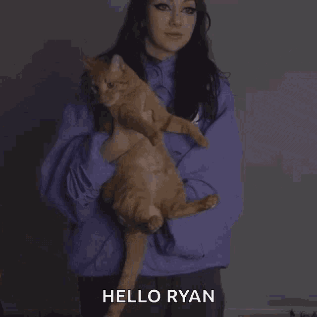 a woman in a purple sweatshirt is holding an orange cat and saying hello ryan .
