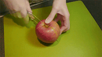 a person is cutting an apple on a cutting board with tweezers .