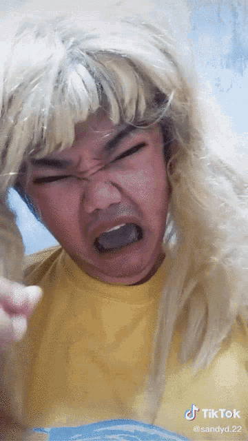 a man wearing a blonde wig and a yellow shirt is making a funny face with the hashtag tiktok at the bottom