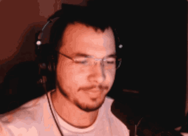 a man wearing glasses and headphones looks at the camera with his eyes closed