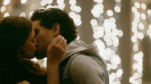 a man and a woman are kissing in front of a string of christmas lights .