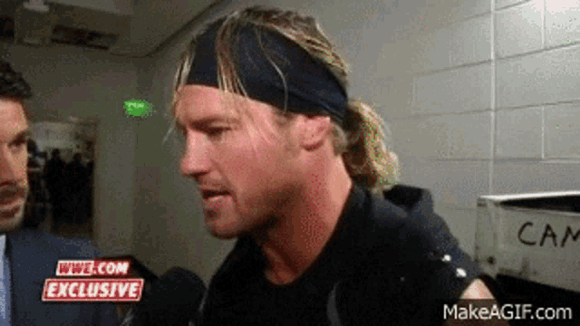 a man wearing a headband is talking to a reporter in a locker room .