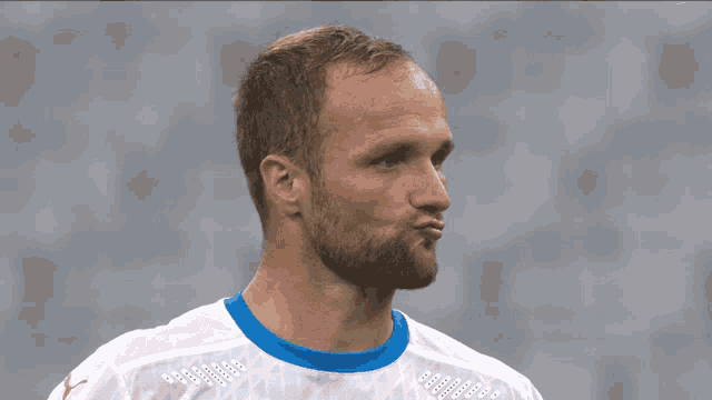 a man with a beard is wearing a white shirt with a blue x on the shoulder
