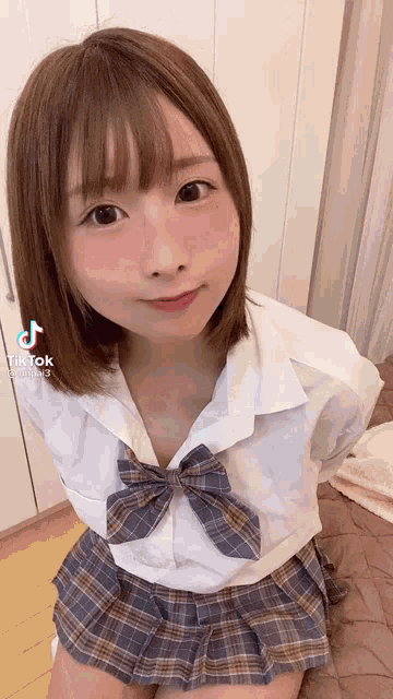 a young girl in a school uniform is sitting on a bed .