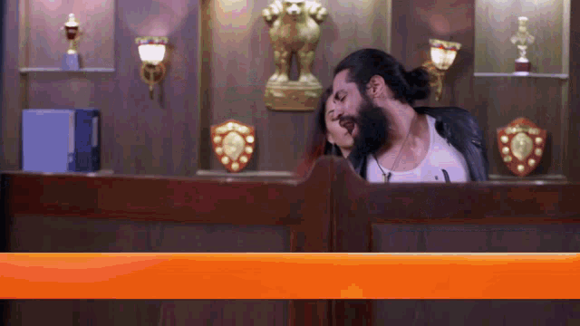 a man with a beard is behind a counter with trophies on the wall
