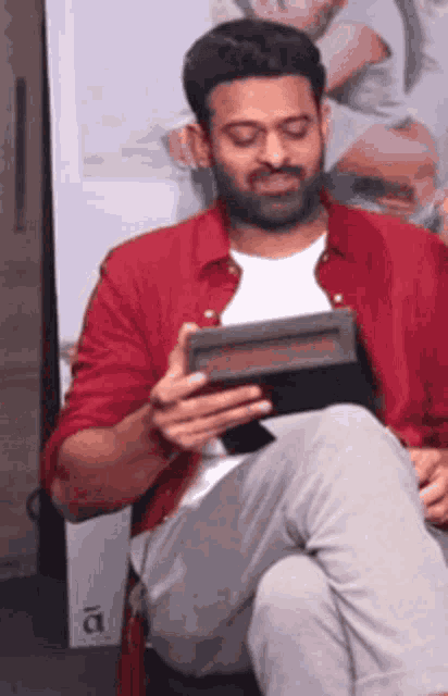 a man in a red shirt is sitting down holding a tablet computer .