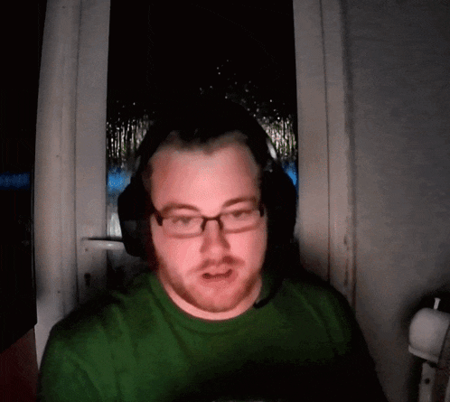 a man wearing glasses and headphones looks at the camera in a dark room