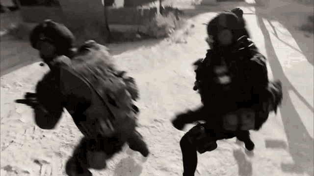 a black and white photo of two soldiers running in the sand
