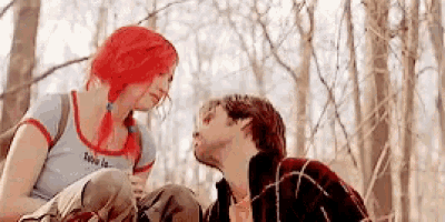 a man and a woman are sitting next to each other in the woods looking at each other .