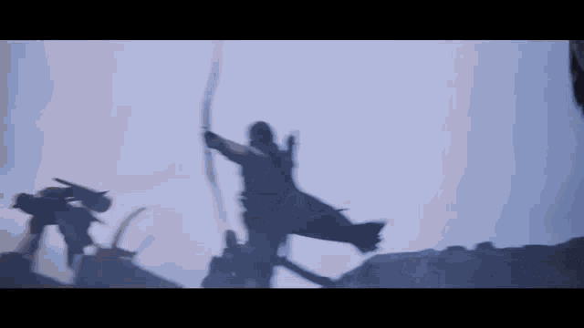 a silhouette of a man holding a bow and arrow against a cloudy sky .