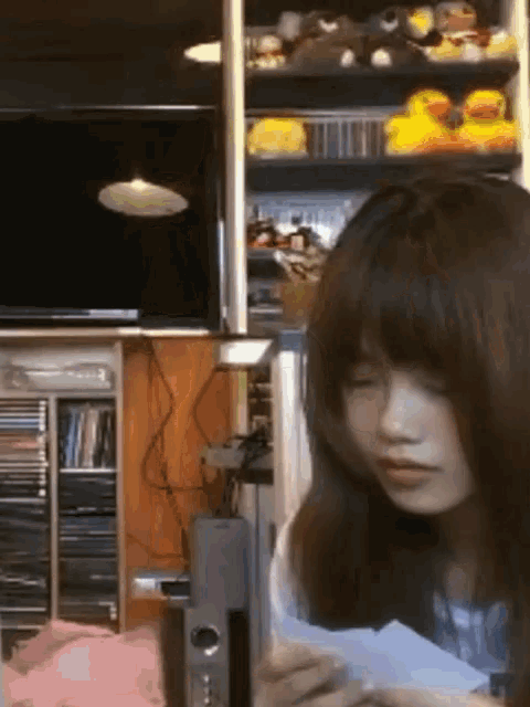 a girl is looking at a piece of paper in front of a shelf full of stuffed animals