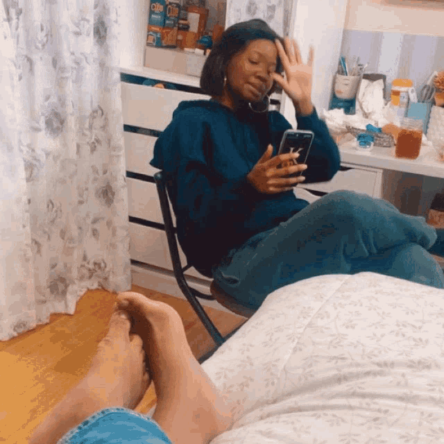 a woman in a blue sweatshirt sits on a chair looking at her phone