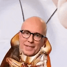 a bald man wearing glasses and a cockroach costume is making a funny face .