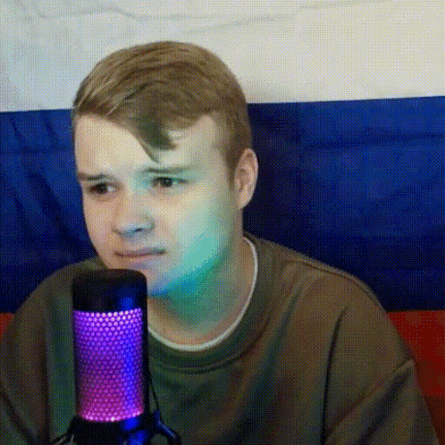 a young man is sitting in front of a microphone with a russian flag behind him .