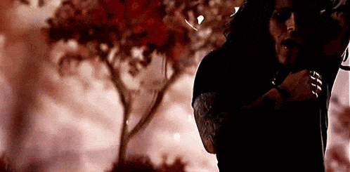 a man with long hair is standing in front of a tree in a dark room .
