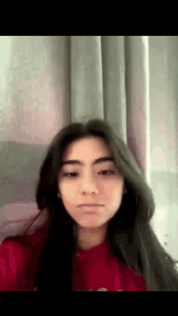 the girl is wearing a red sweatshirt and looking at the camera .