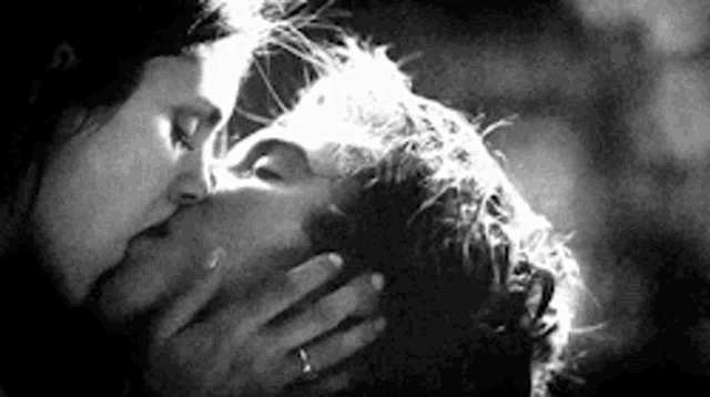 a black and white photo of a man and woman kissing each other .