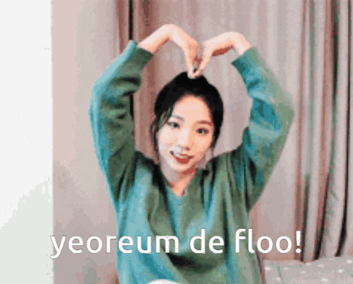 a girl in a green sweater is making a heart shape with her hands