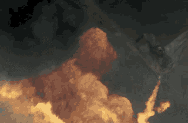 a plane is flying through a cloudy sky with a huge explosion in the background