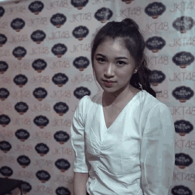 a woman in a white shirt stands in front of a wall with jkt48 written on it