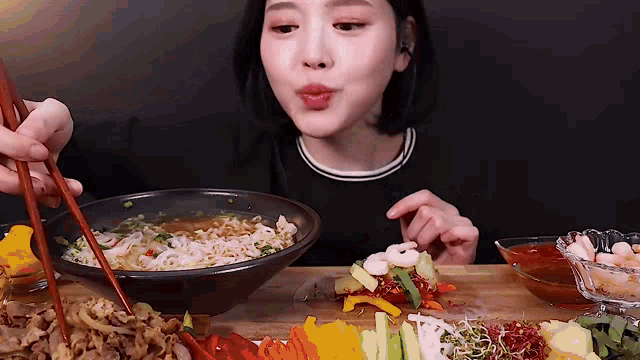 a woman is eating a bowl of ramen with chopsticks and a plate of food .