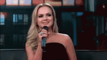 a woman in a black dress is holding a microphone in her hand and smiling .
