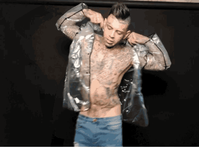 a shirtless tattooed man wearing a clear plastic raincoat