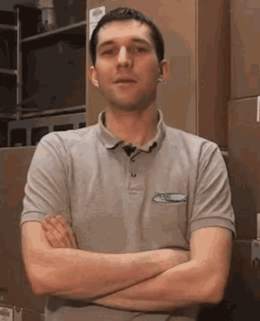a man with his arms crossed wears a grey shirt with a ford logo on the pocket