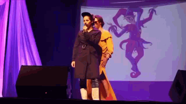 a man is standing on a stage holding a microphone while a woman is standing behind him .