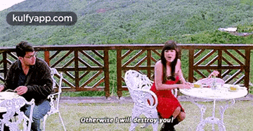 a man and a woman are sitting at a table on a balcony and the woman is talking to the man .