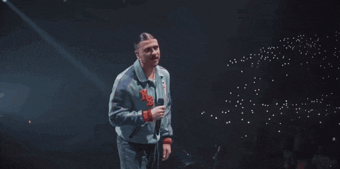 a man singing into a microphone with the letter s on the front of his jacket