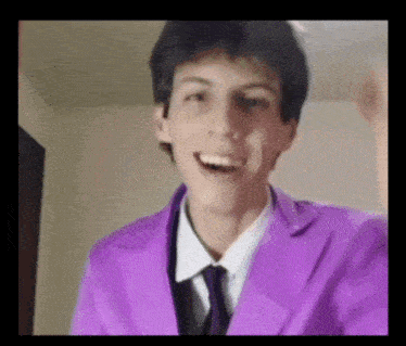 a young man wearing a purple suit and tie is smiling and making a funny face .