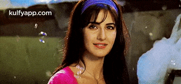 a woman wearing a pink top and a blue headband is looking at the camera .