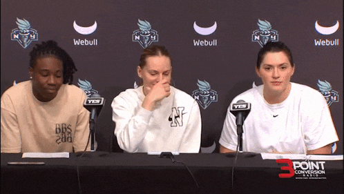 three women sit at a table in front of a webull sign
