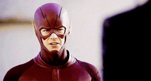 a man in a flash costume is standing next to another man in a suit .