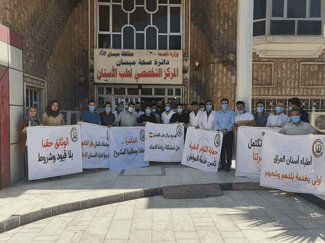 a group of people holding signs in front of a building that says ' وزارة الصحة ' on it