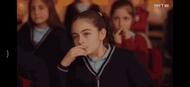 a group of young girls are sitting in a classroom and one of them is covering her nose with her hand