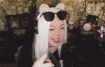a woman wearing a cat ear headband and sunglasses is pointing at the camera .