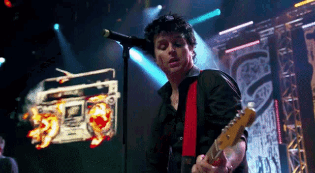 a man playing a guitar and singing into a microphone on a stage .