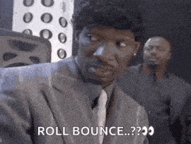 a man in a suit and tie is saying `` roll bounce ... '' while another man stands behind him .