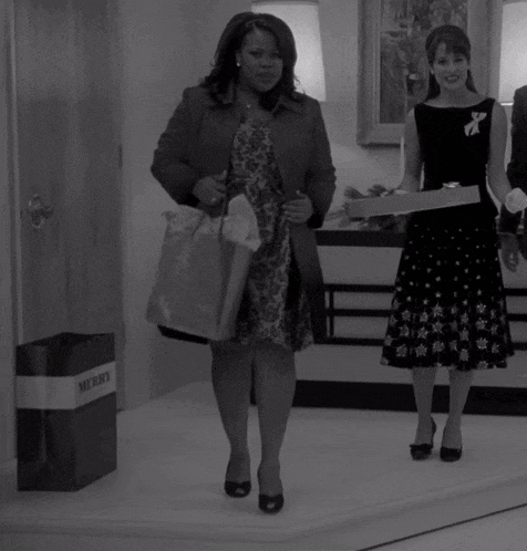 a black and white photo of two women with a merry bag in the background