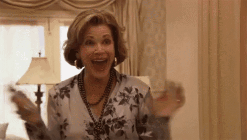 a woman in a floral shirt and necklace is holding a remote control in her hand .
