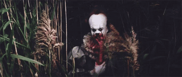 a clown with blood on his face is in the grass