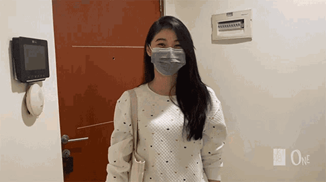 a woman wearing a mask is standing in front of a door that says one